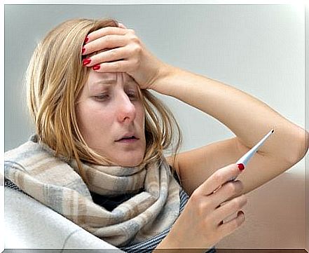 Woman holding her head and a thermometer