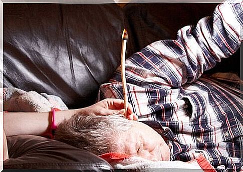 Man lies on the couch with a burning ear candle in his ear