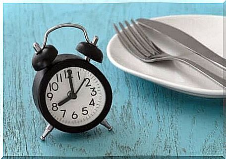 An alarm clock on a table next to a plate and cutlery